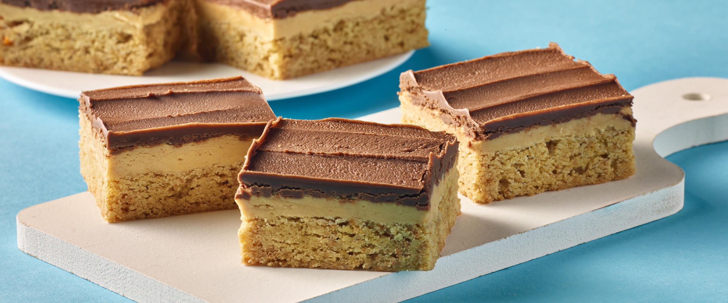 Three chocolate graham bars sitting on a wooden board on top of a teal bakground.