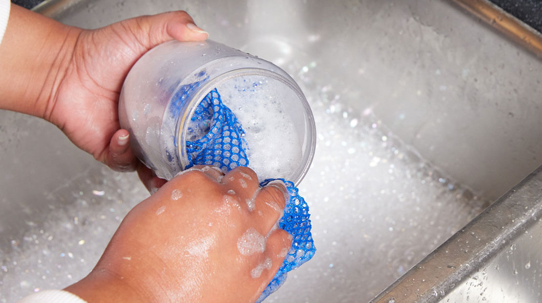 hands washing a peanut butter jar out with soap