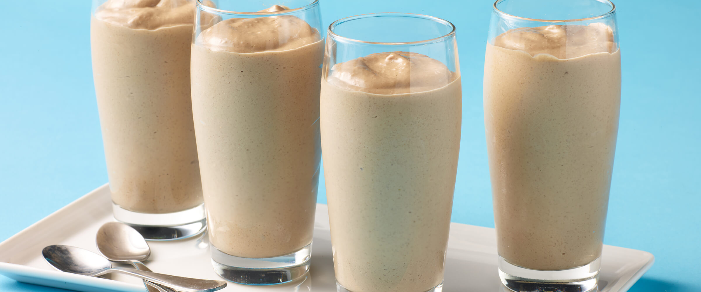 Four glasses containing smoothie on a plate