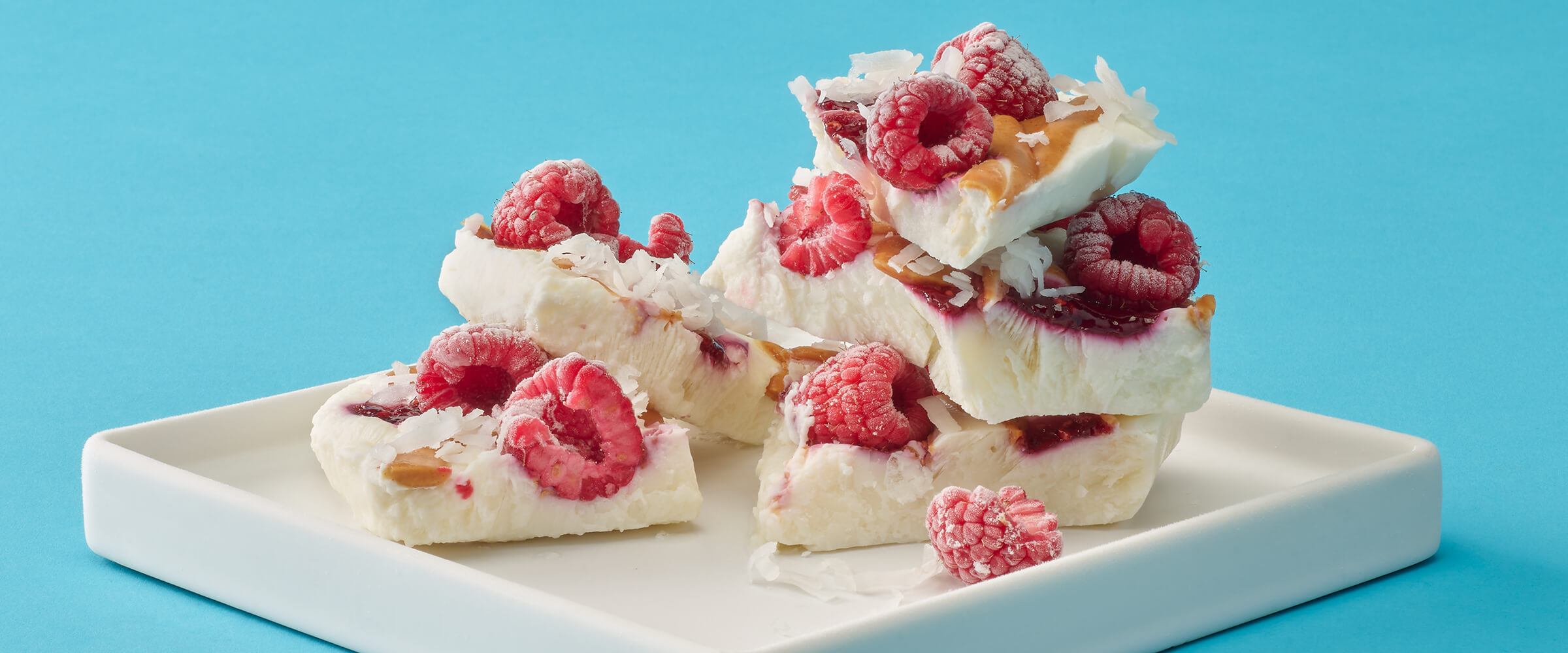 White frozen yogurt bark with raspberries and peanut butter drizzle on a white square plate