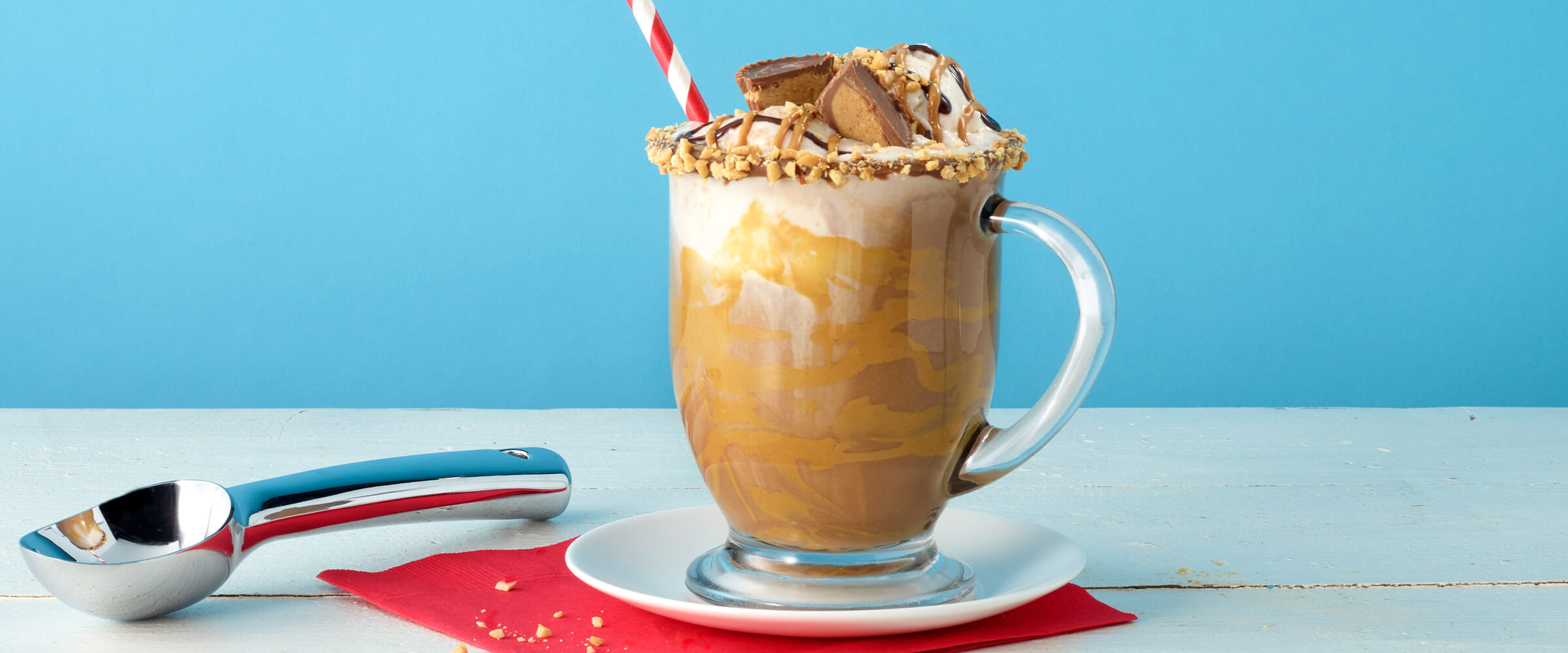 Peanut butter hot chocolate float in a tall glass mug sitting on a white plate