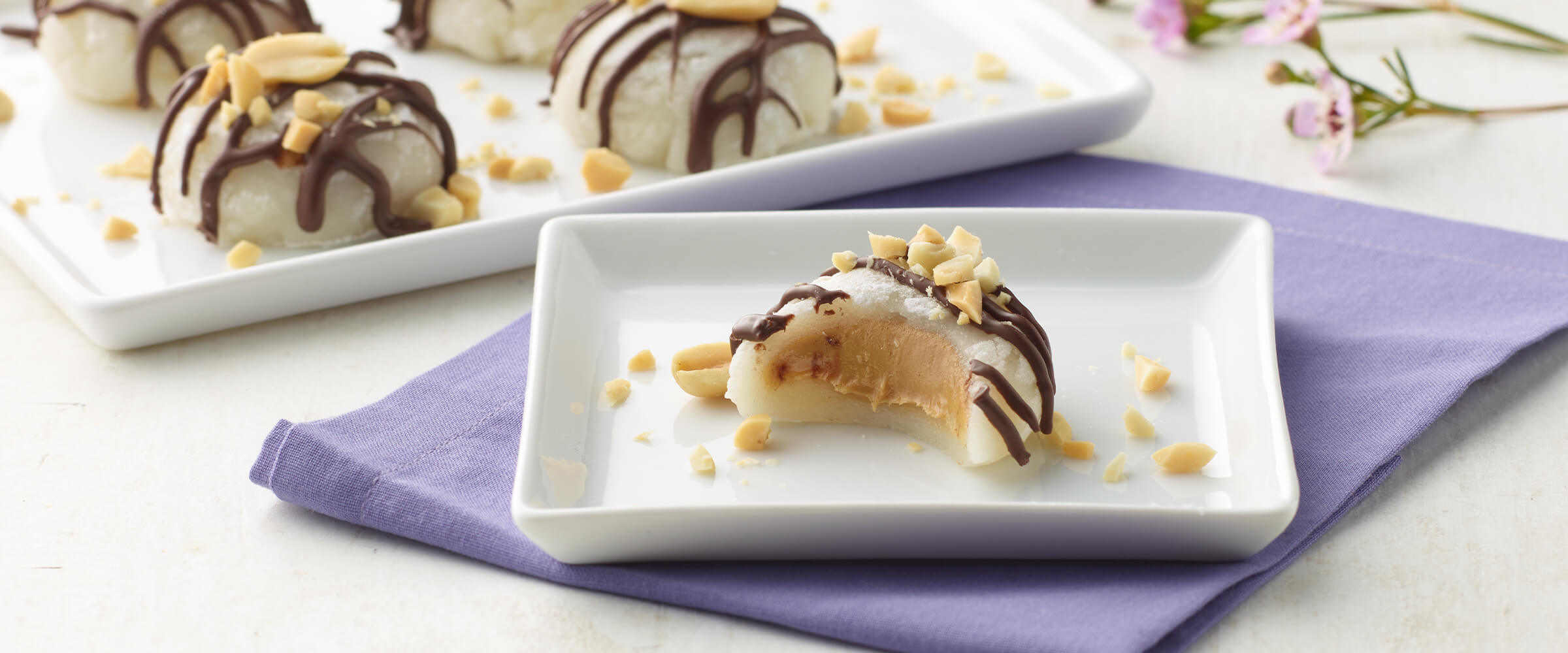 Peanut butter mochi on a small white, square plate on top of a light purple napkin