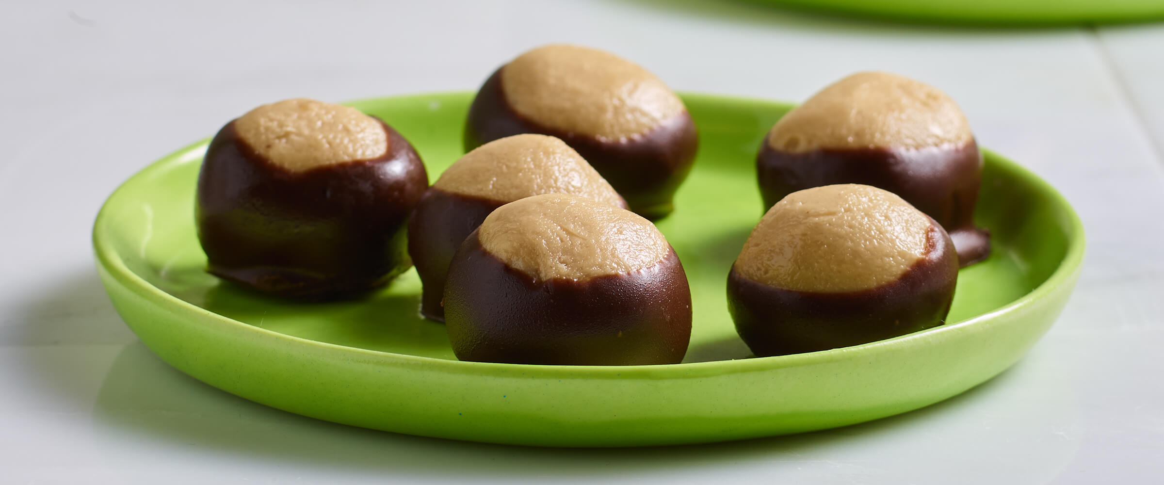 Six buckeyes on a small lime green plate sitting on a white countertop.