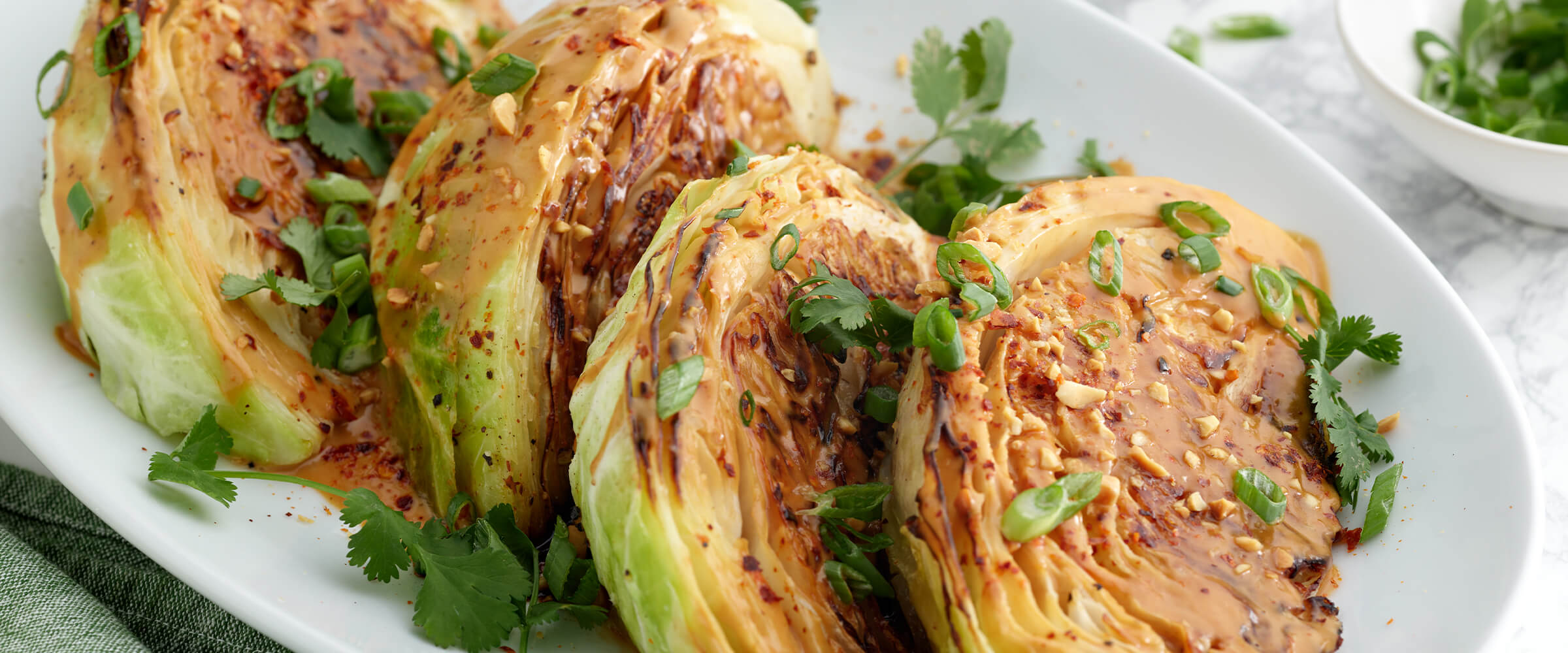 Charred cabbage with peanut sauce on a large white serving platter with garnishes of cilantro and green onion.