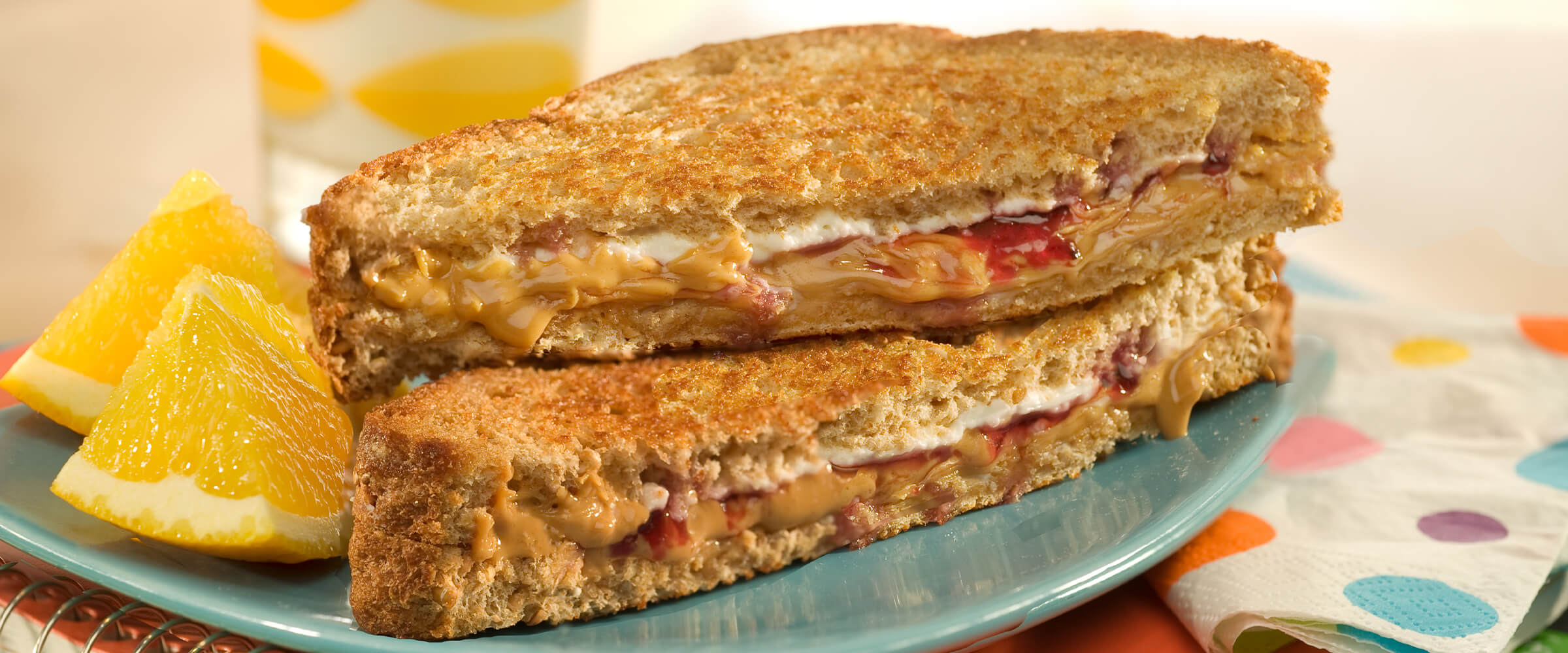 A creamy grilled peanut butter and jelly sandwich cut in half on a teal plate with two orange slices next to it.