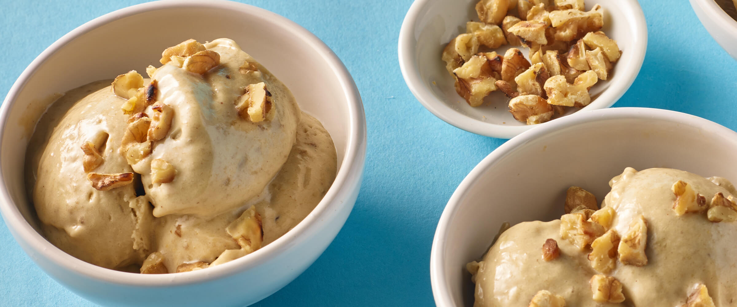 Two bowls of easy banana and peanut butter ice cream with a small bowl of crushed peanuts on a teal background.