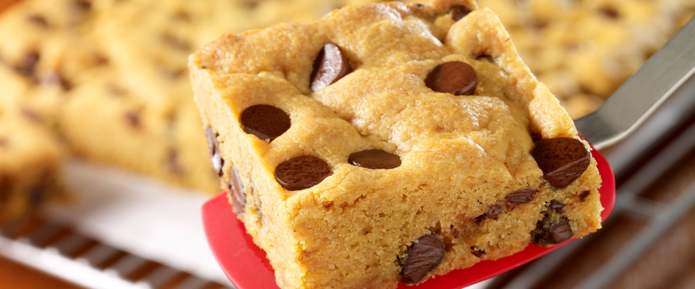 Peanut butter cookie bar sitting on a red spatula in front of a tray of other cookie bars