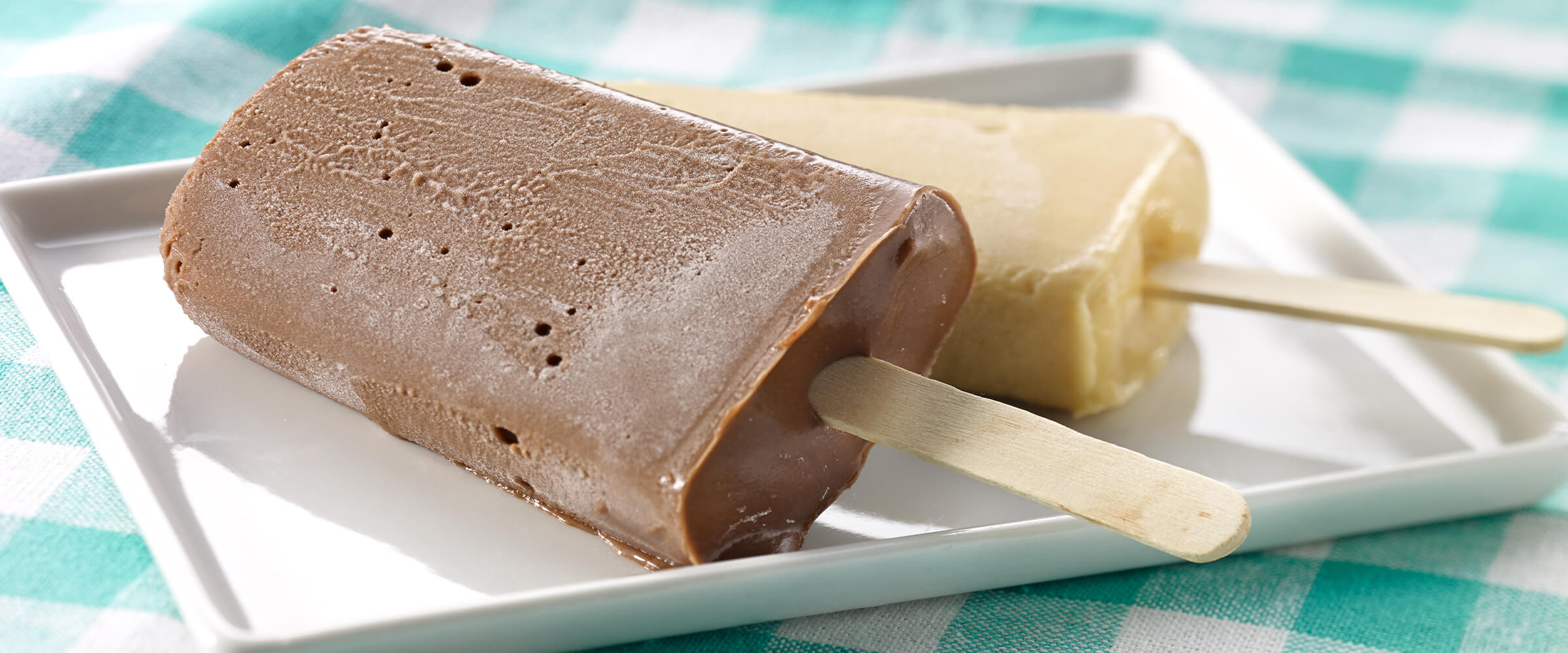 Two frozen peanutty pops resting on each other on a square white plate.