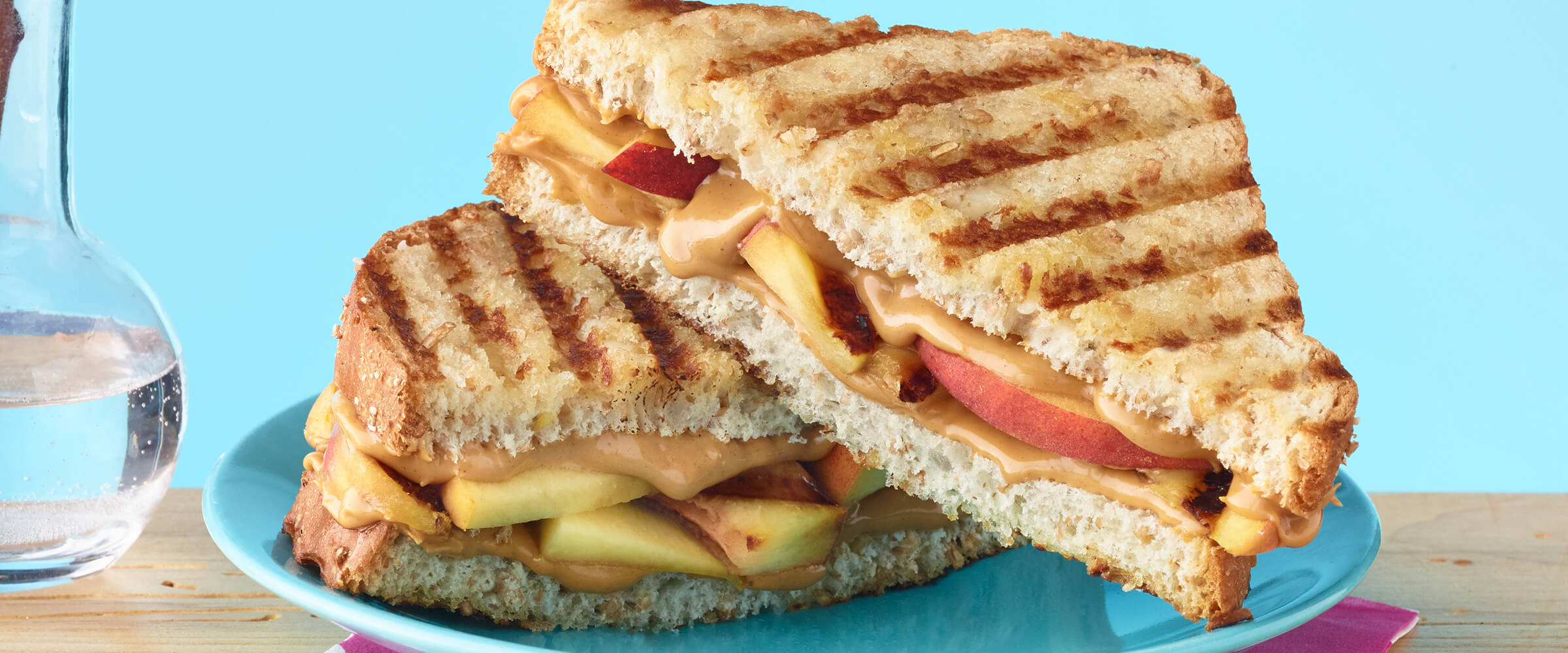A grilled peanut butter and peach sandwich cut in half, sitting on a teal plate on a wooden table.