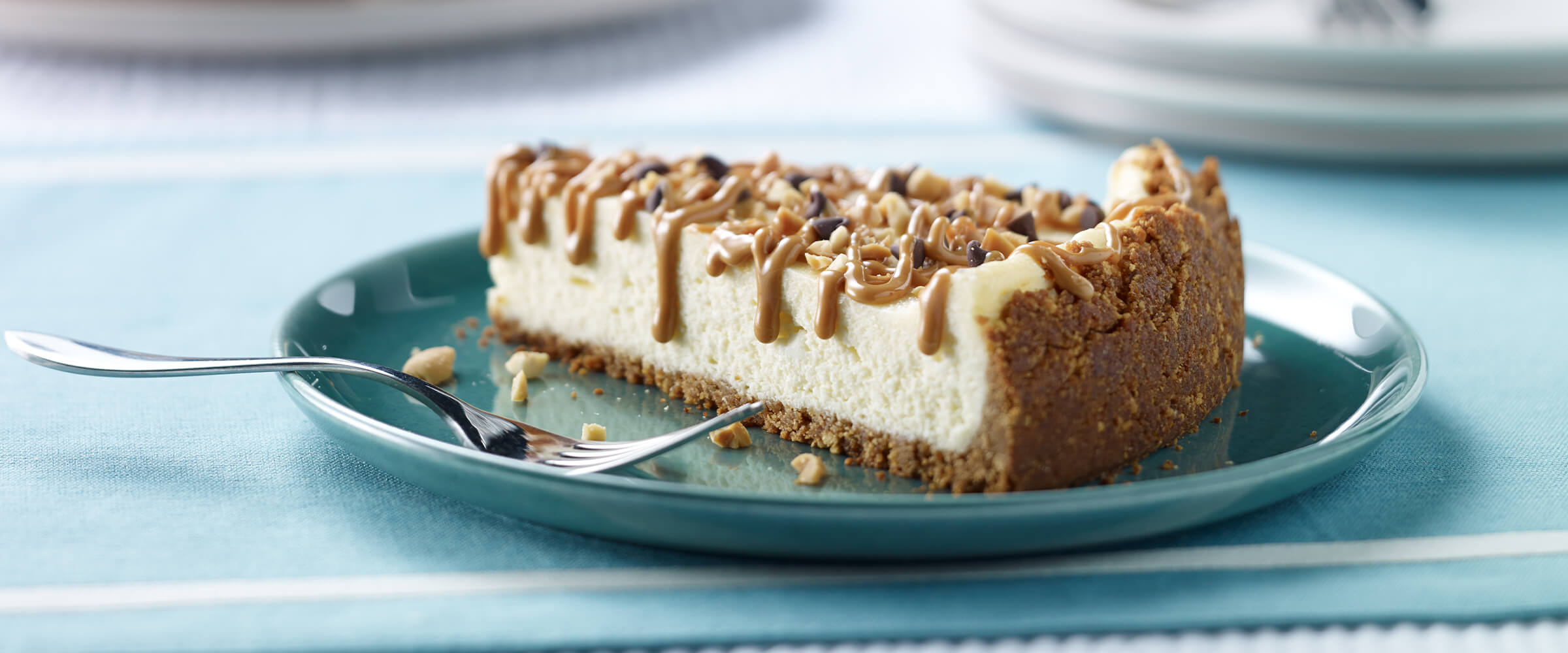A slice of NY-Style Cheesecake on a teal plate with a fork sitting next to it.