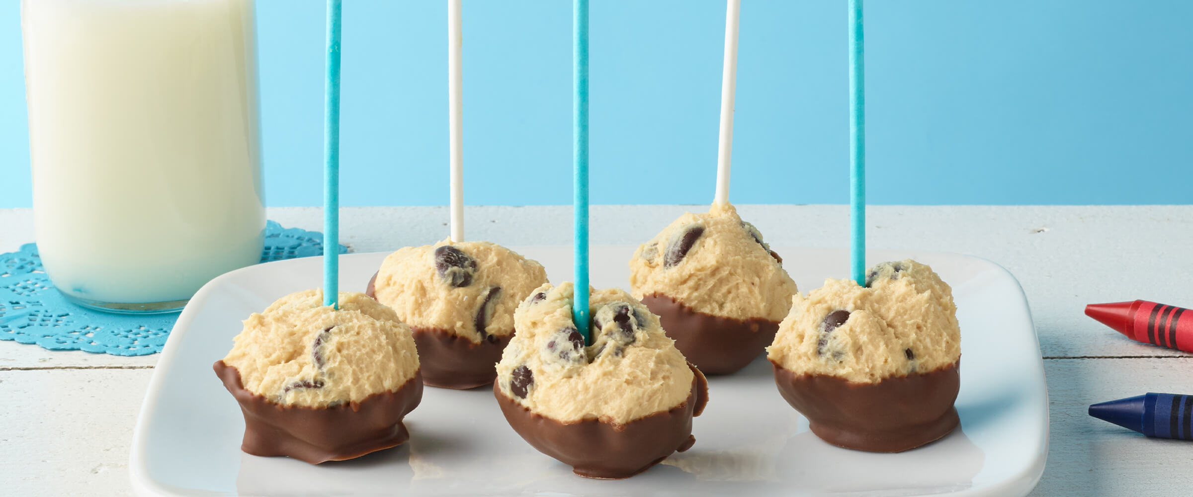 Five no-bake cheesecake pops with alternating teal and white sticks in each one on a white plate.