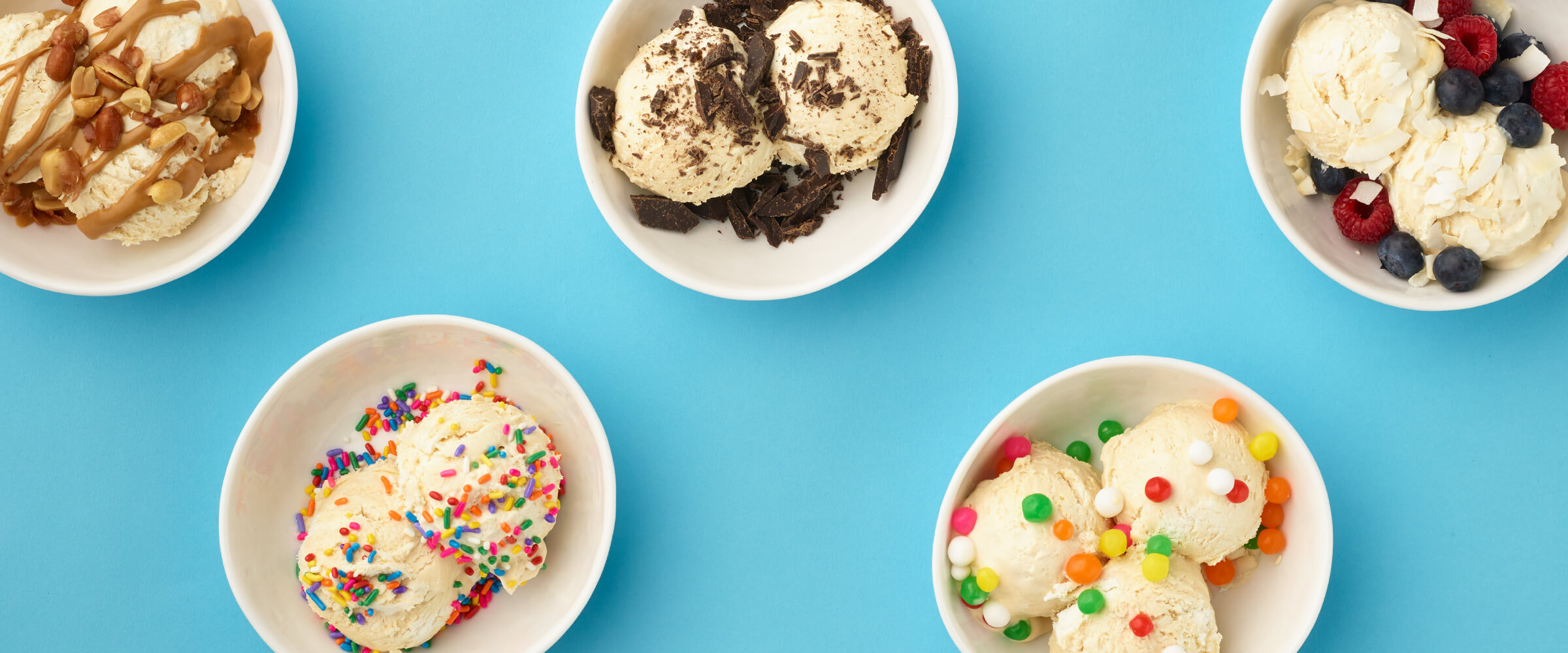 Five white bowls of no-churn peanut butter ice cream with various toppings including chocolate cookies, melted peanut butter, candy and sprinkles.