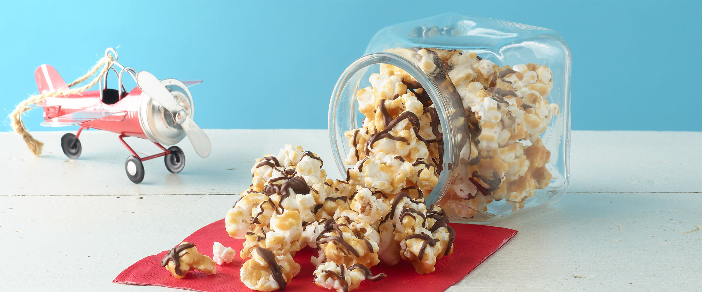 a tipped over jar of popcorn coated in a drizzle of peanut butter caramel and chocolate
