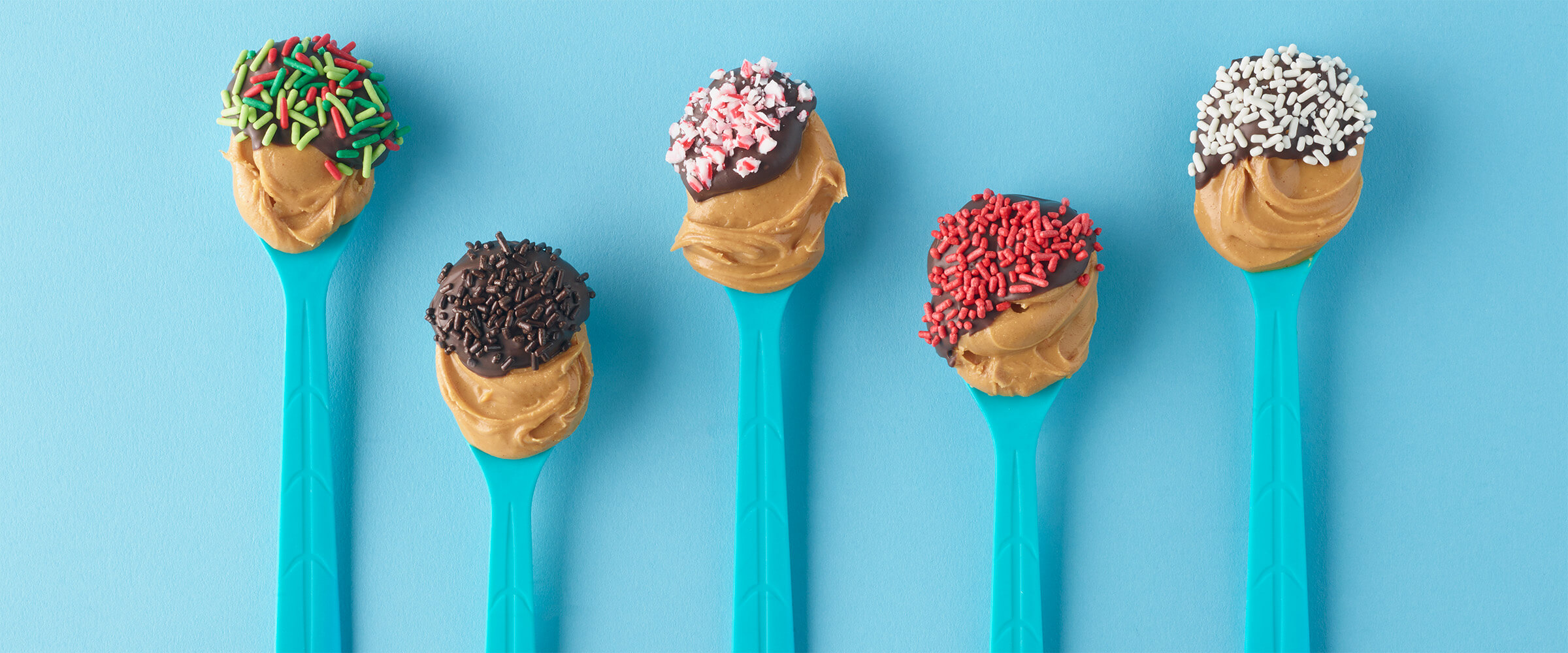 Spoons of peanut butter with chocolate dipped in various toppings