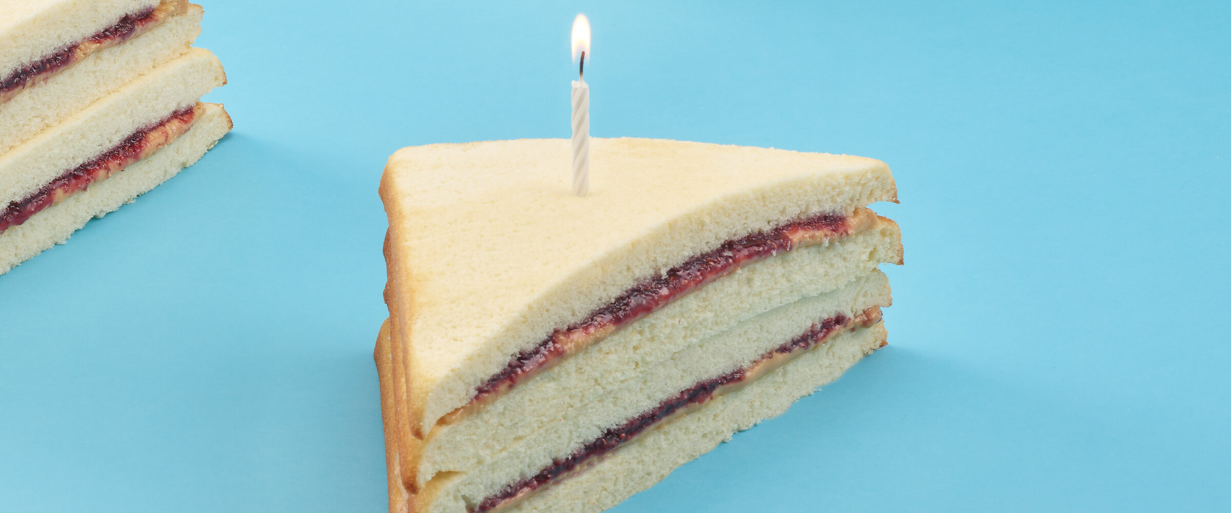 A slice of Pb and J cake with a lit birthday candle in the center of the slice.