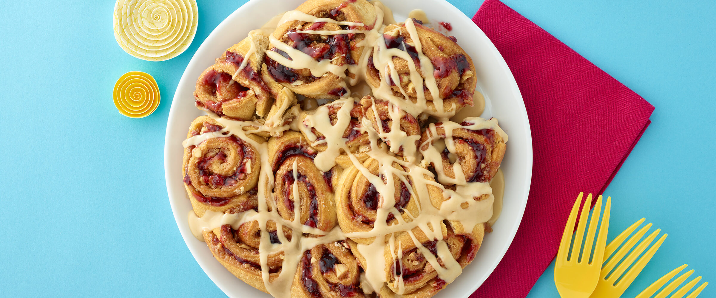 Peanut butter and jelly rolls on a large white serving plate sitting on a teal background with yellow forks off to the right.