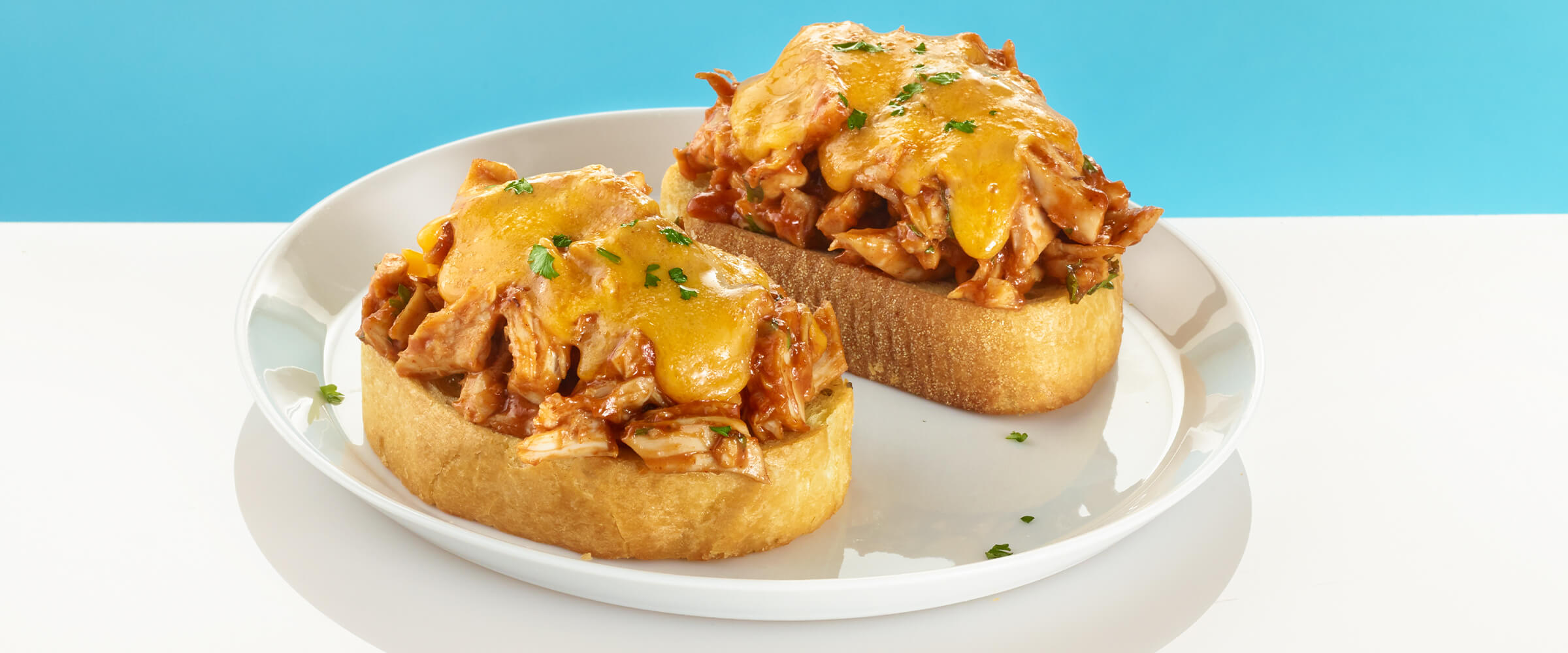 Two peanut butter BBQ chicken melts on a white plate with a teal background behind them.