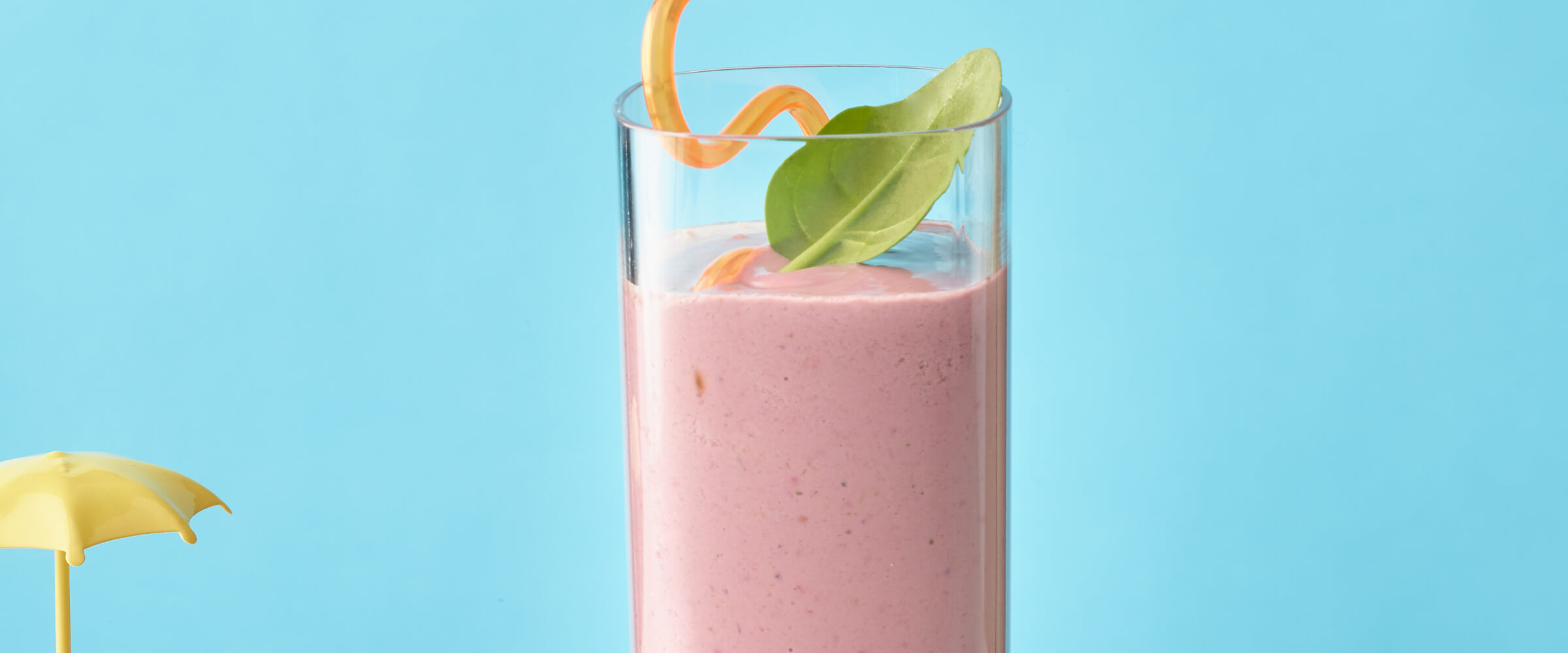 Peanut butter black berry smoothie in a tall narrow glass with an orange bendy straw and a sprig of mint on a teal background.