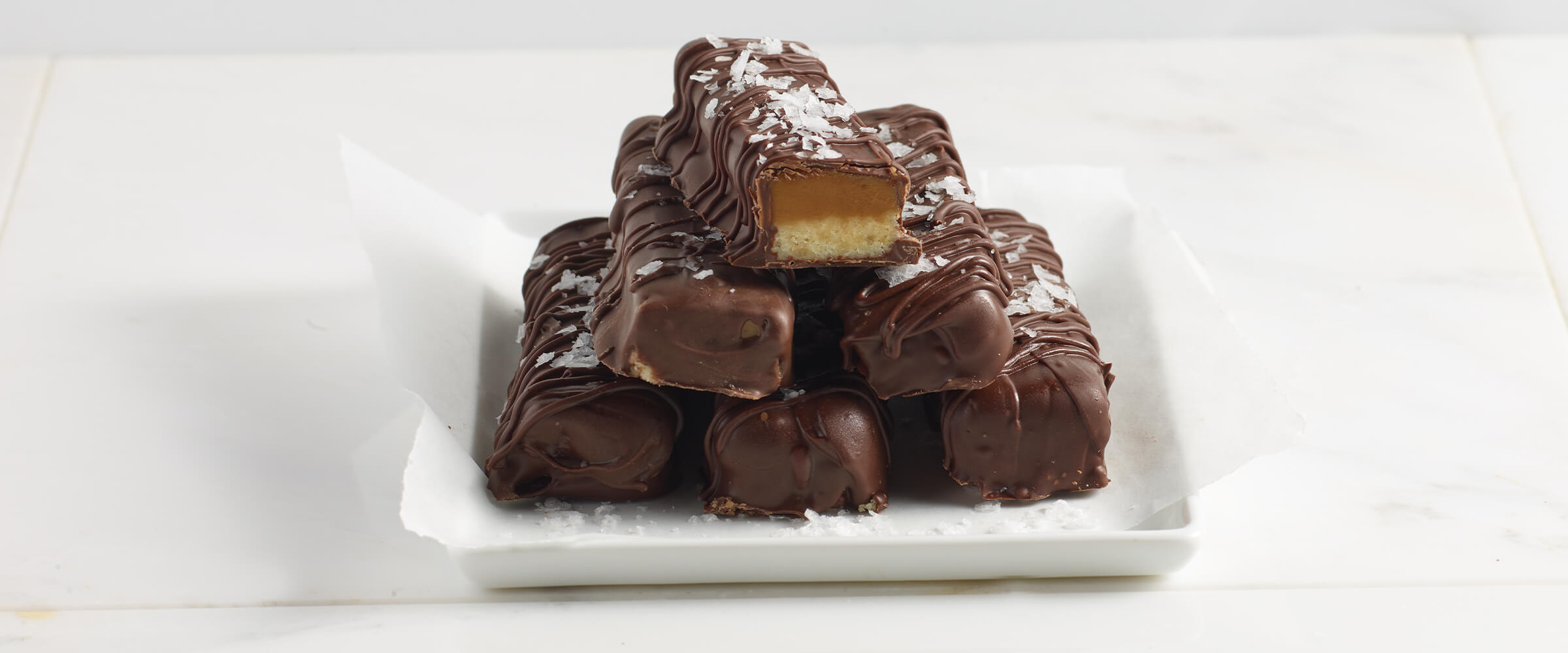 Peanut butter caramel bars stacked on top of each other on a small square white plate