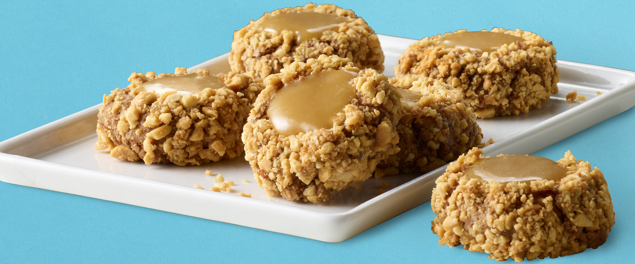 Peanut butter caramel thumbprint cookies stacked on a small white square plate.