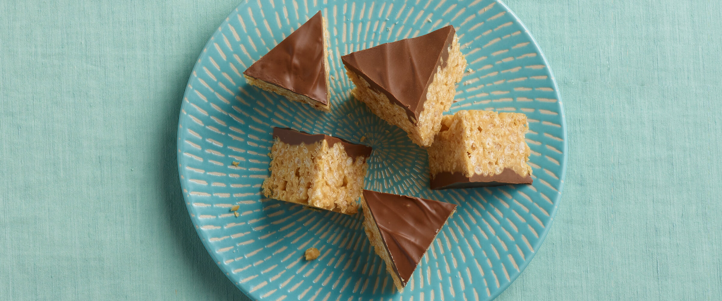 Peanut butter cereals bars cut into small triangles on a small teal and white plate.