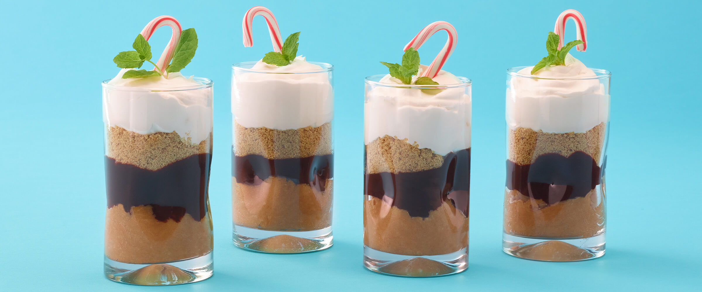 Four cheesecake peanut butter parfaits on a teal background.
