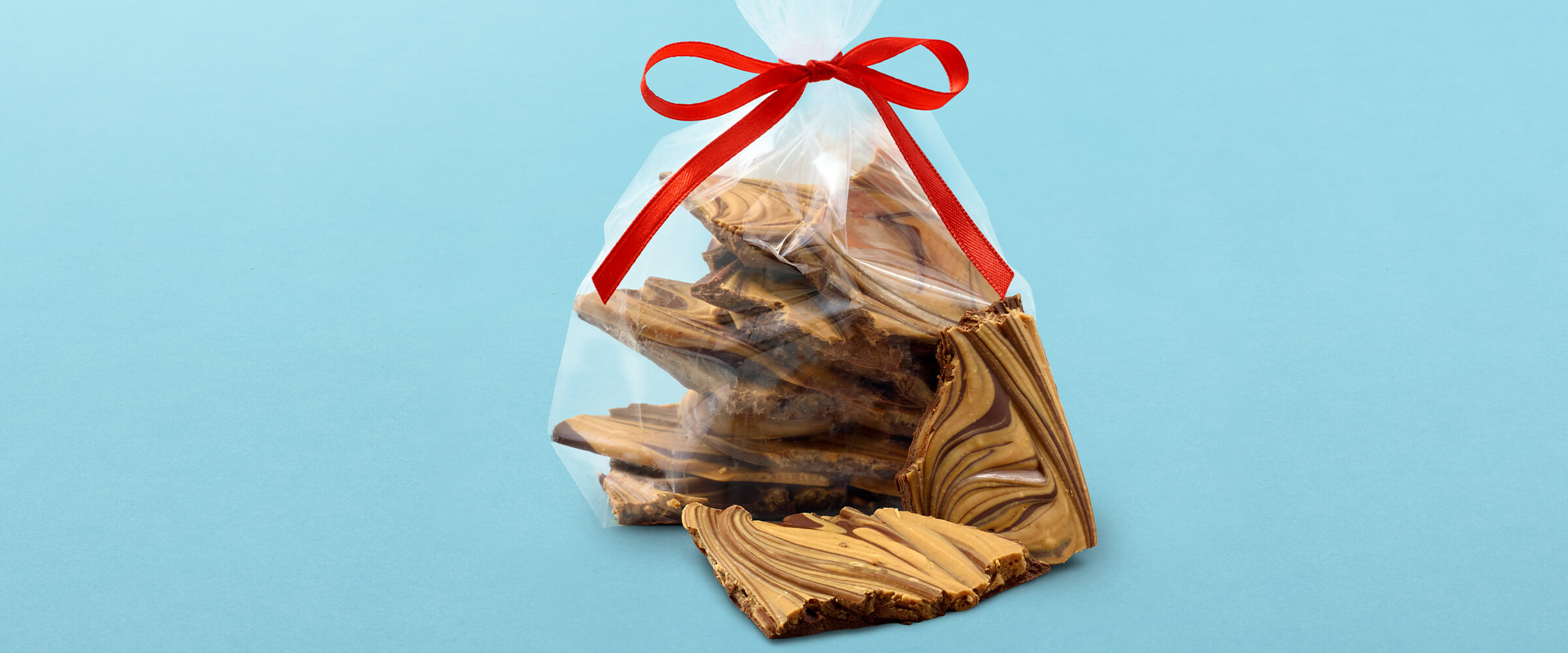 Pieces of peanut butter chocolate swirl bark in a plastic bag tied with a red ribbon on a teal background