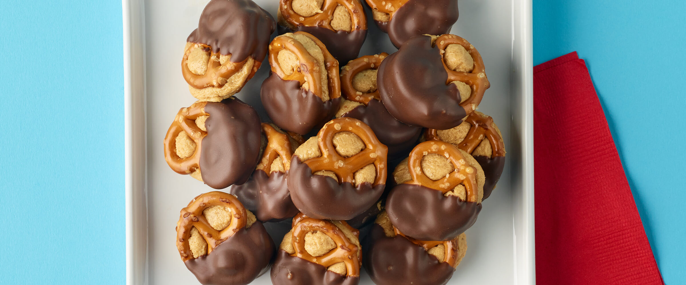 Peanut butter pretzel bites stacked on top of each other on a square white plate with a red napkin tucked underneath