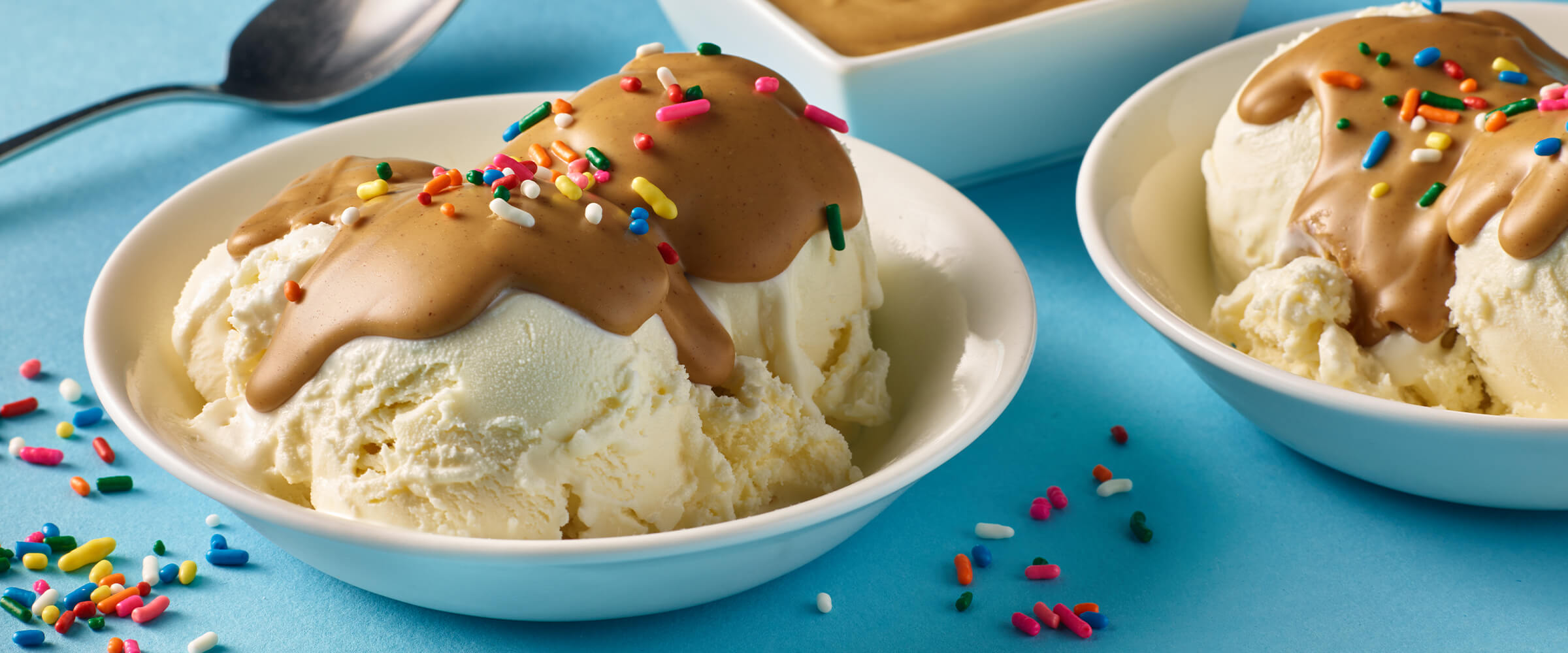 Two white bowls of vanilla ice cream with melted peanut butter and sprinkles on top.