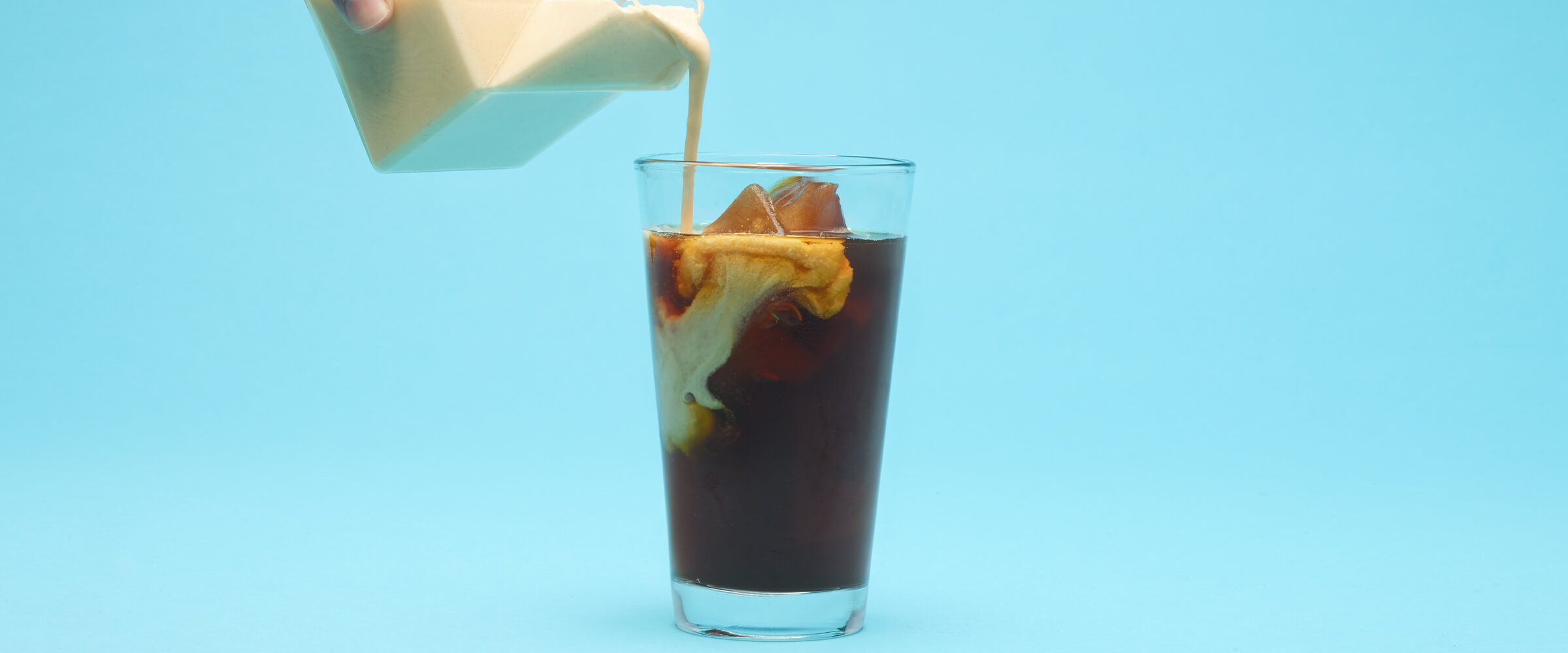 Peanut butter cream being poured into a glass of iced coffee with a teal background.