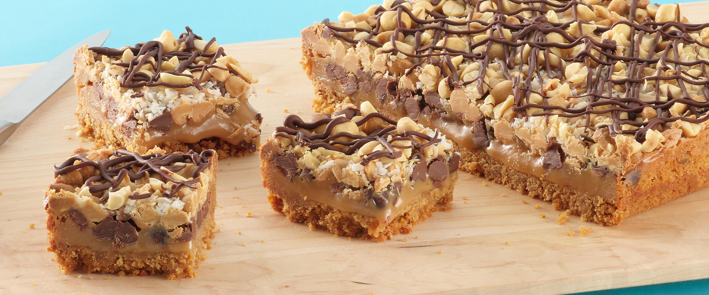 Three peanut butter magic cookie bars next to a full slab of uncut bars on a wooden board.