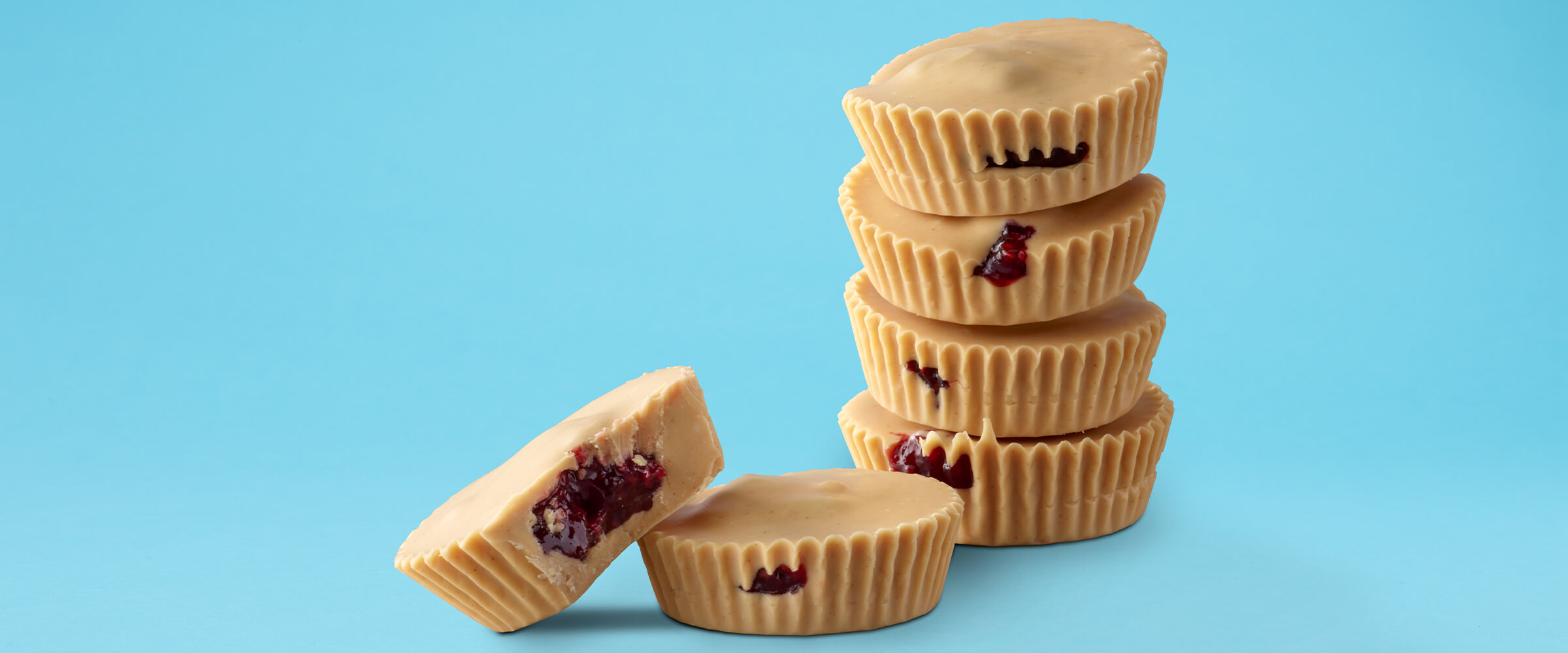 Four peanut butter raspberry cups stacked on top of each other with two cups in front of them on a teal background.