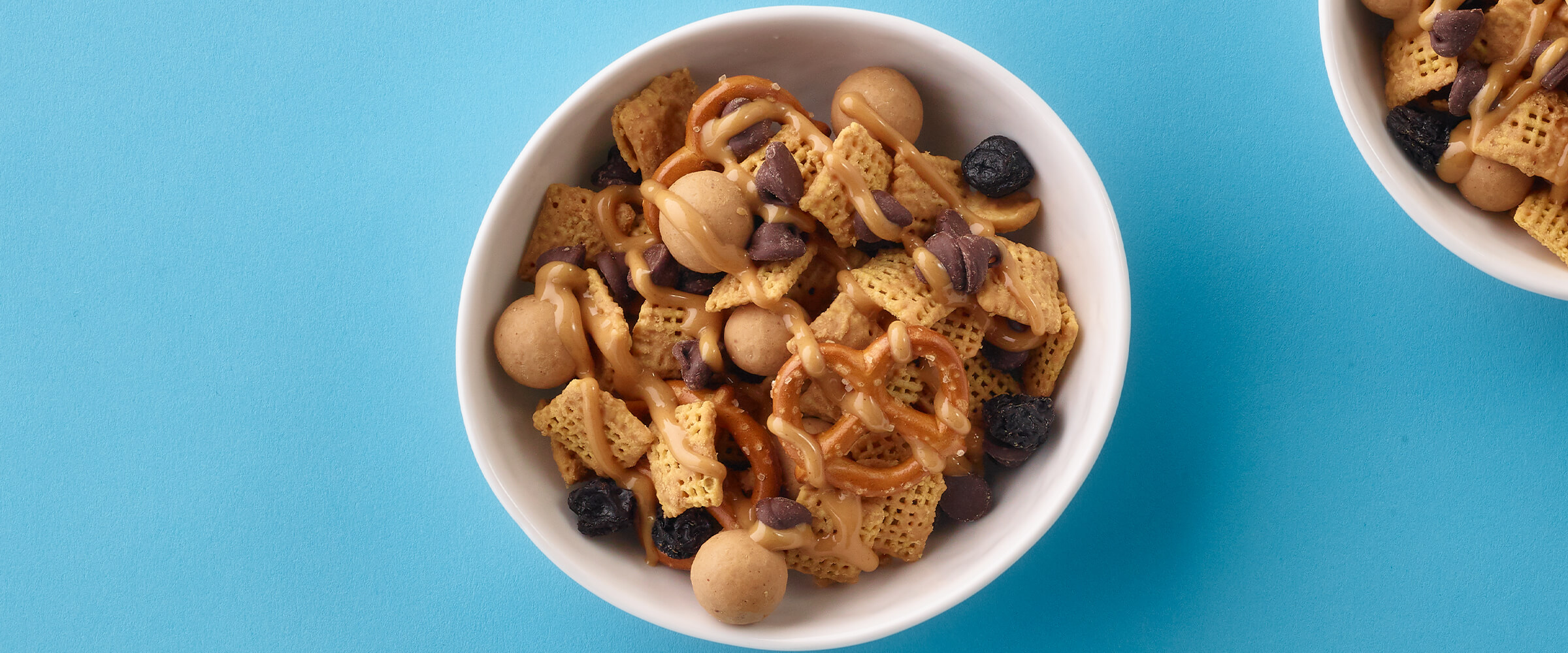 Two small teal bowls of peanut butter snack mix on a teal background.