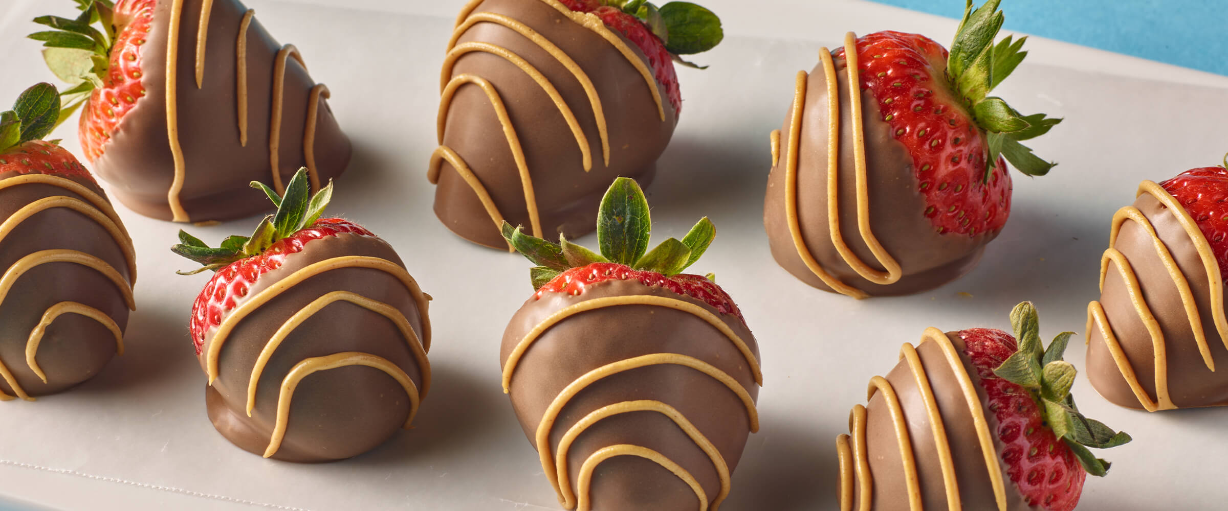 Eight peanut butter and choocolate dipped strawberries on a white, glass serving board.