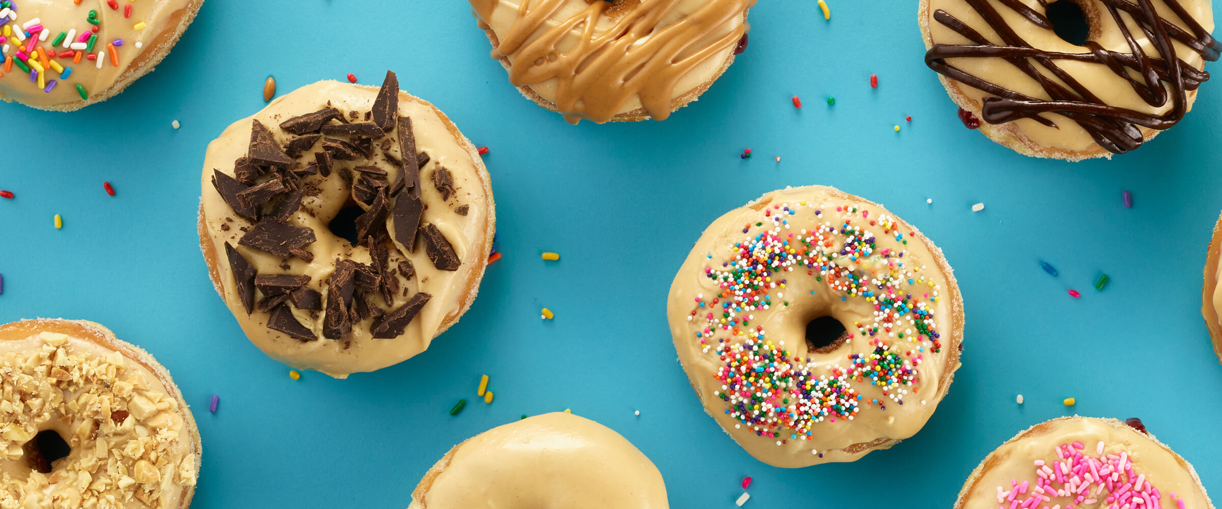 Peanut butter and jelly donuts with various toppings on a teal background.