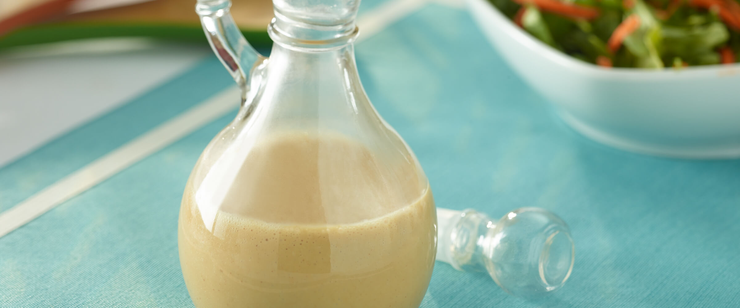 Peanut vinaigrette in a glass bottle on a teal table cloth.