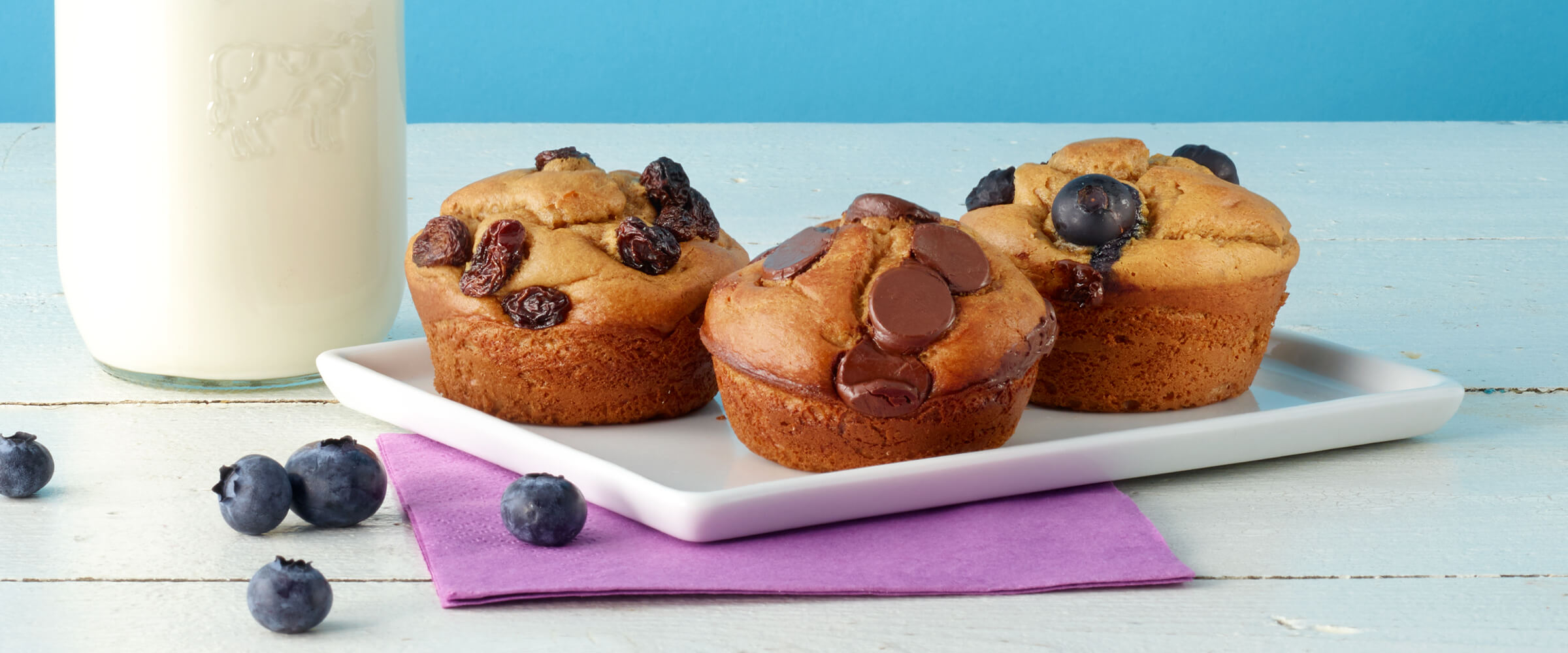 Three flourless peanut butter chocolate chip muffins on on a small white plate sitting next to a jar of milk