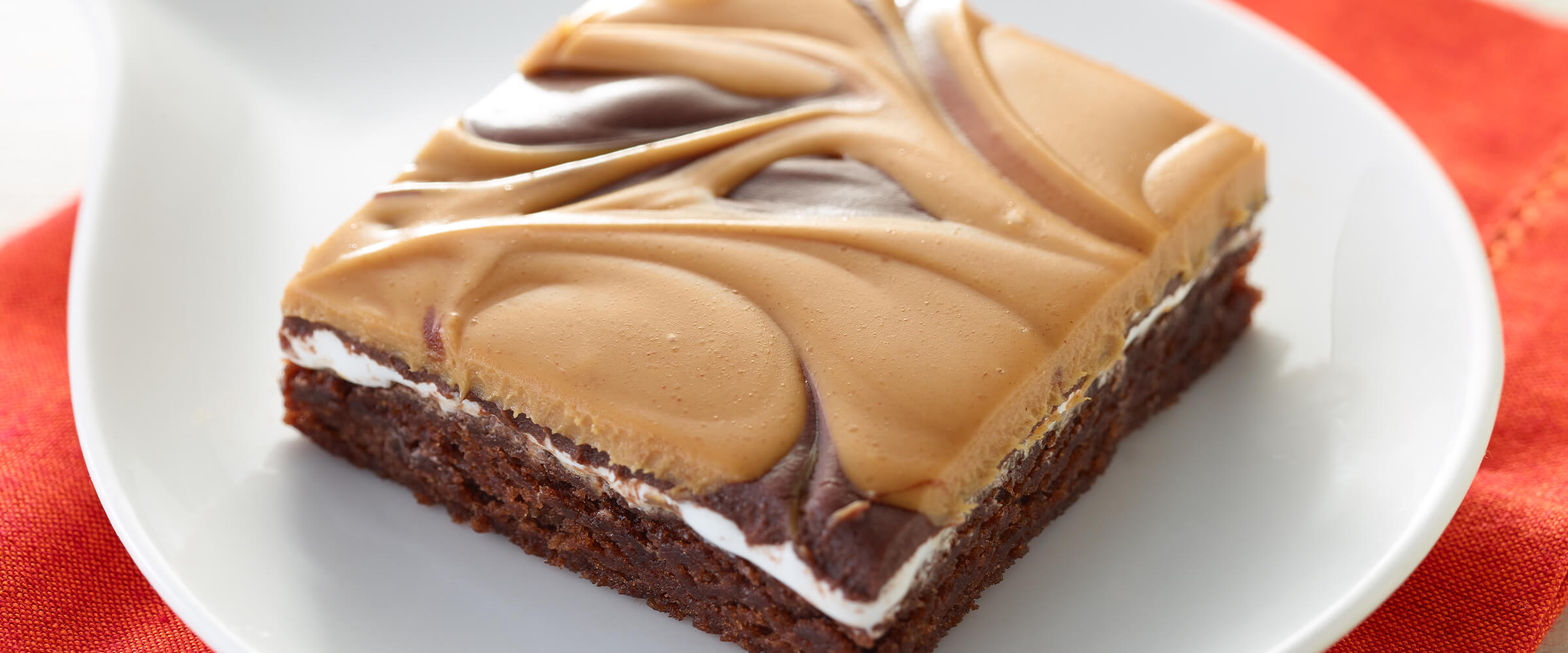 A dreamy brownie sitting on a small white plate on a red-orange napkin.