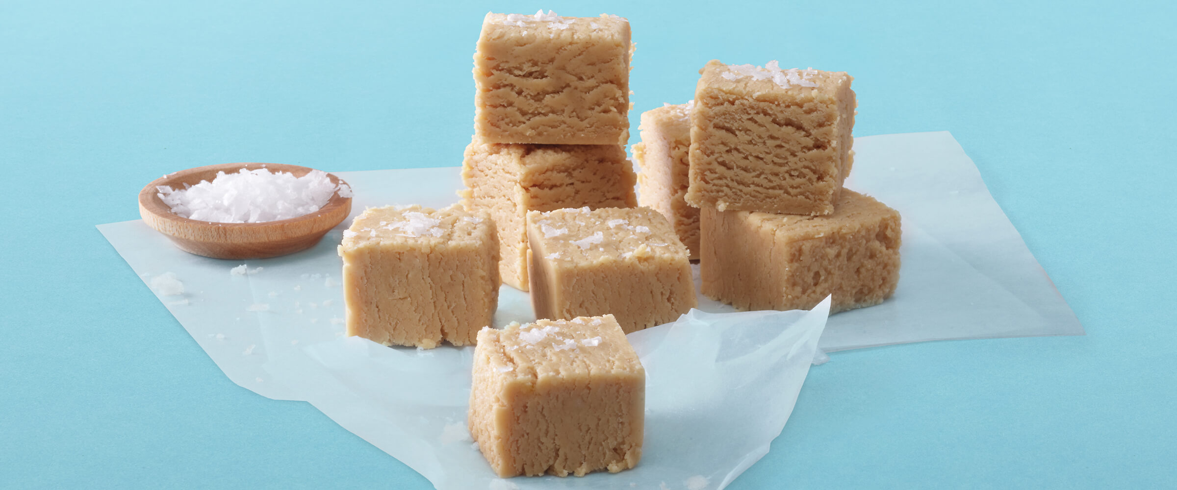 Blocks of peanut butter fudge on parchment paper with a small dish of sea salt sitting next to them