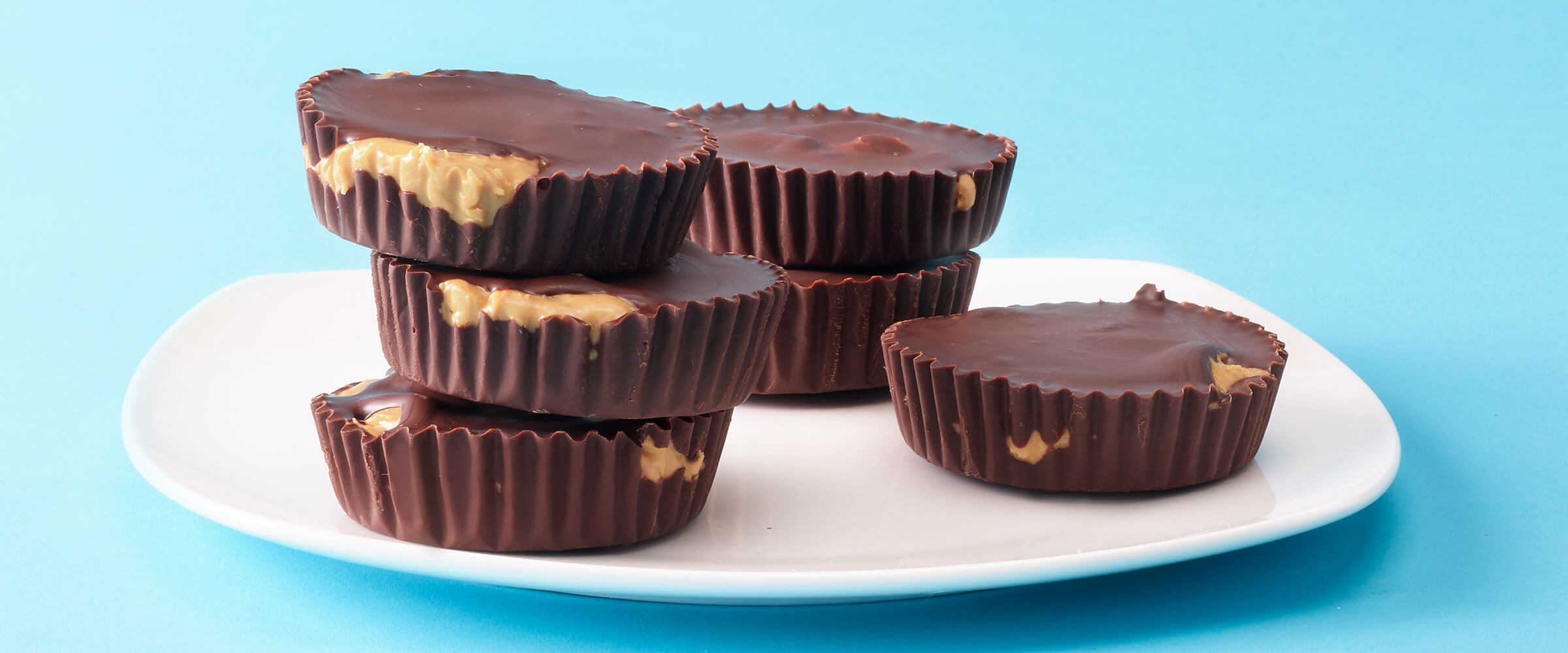 Six SKIPPY® peanut butter cups stacked on a small white plate on a teal background