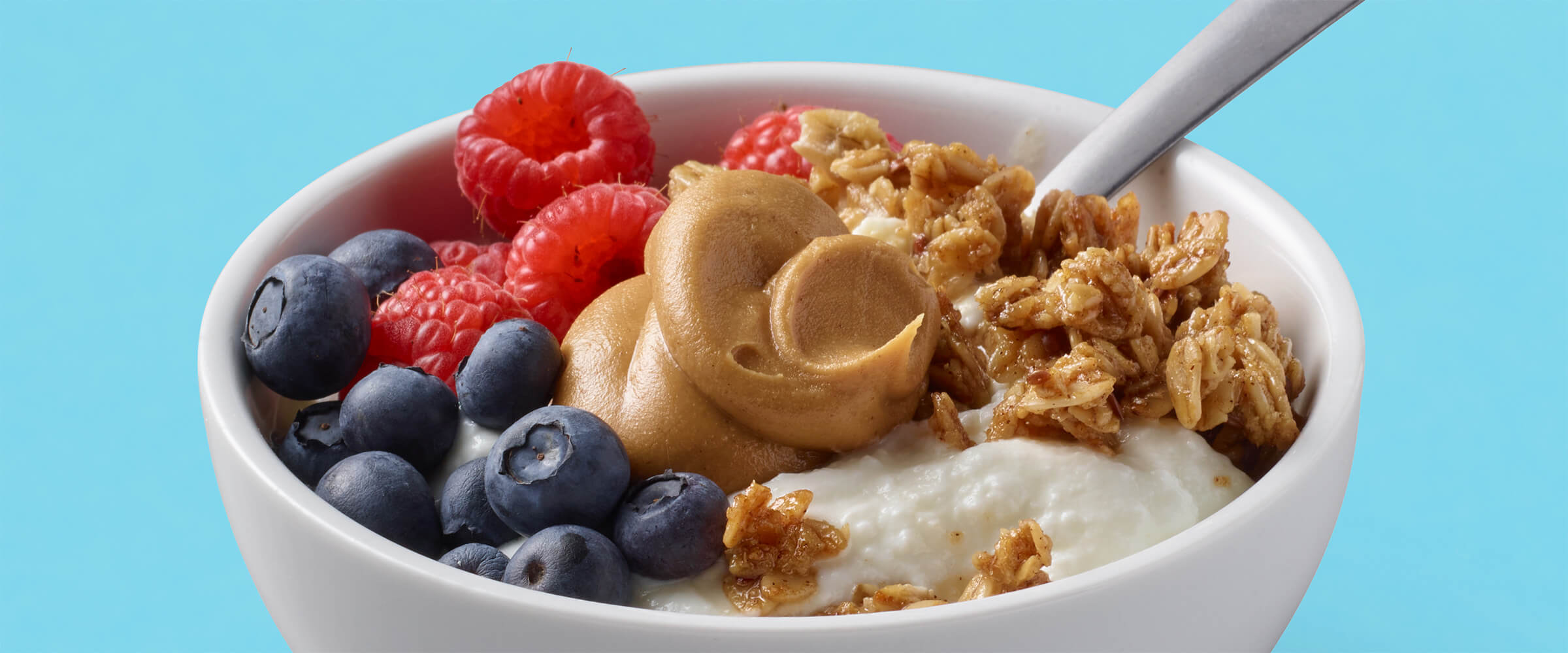 a bowl with yogurt, berries, granola and a spoonful of peanut butter