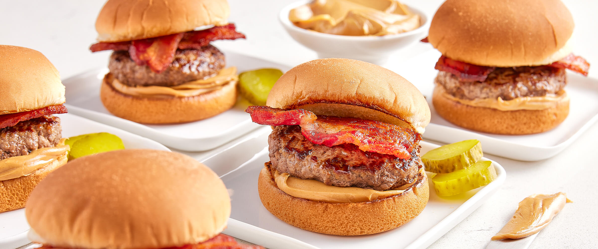 Peanut butter bacon burger sliders with slices of pickle on a square white plate