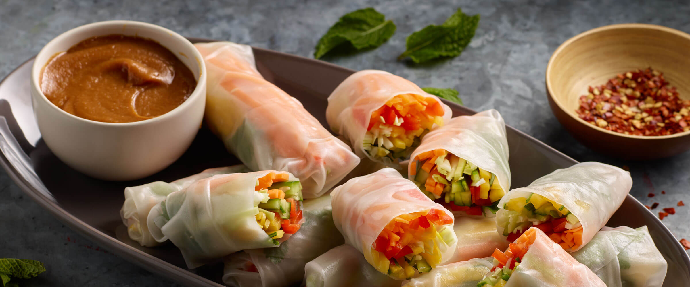 summer rolls on a plate with a bowl of peanut butter dipping sauce