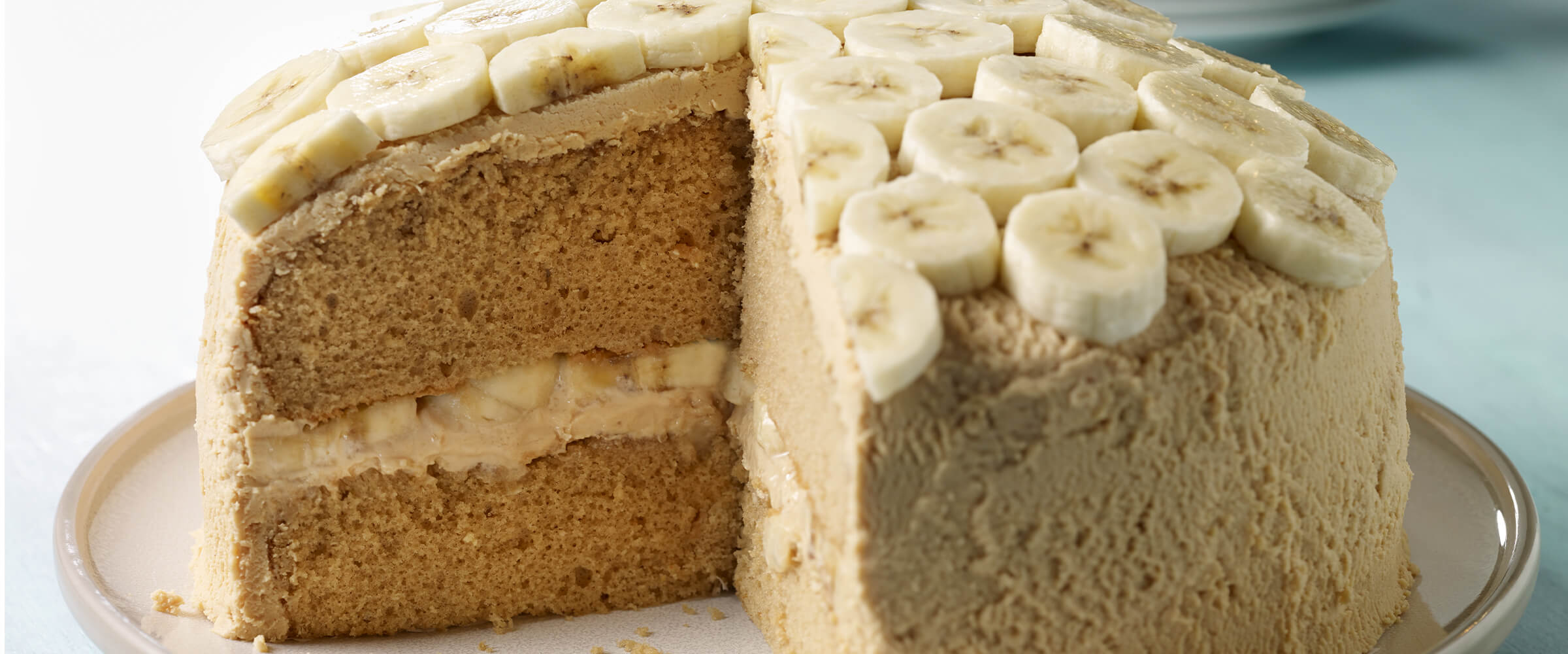Caramel peanut butter cake sitting on a cream-colored plate with a large slice taken out of it.
